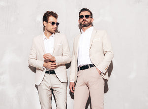 Portrait of two handsome confident stylish hipster lambersexual models. Sexy modern men dressed in white elegant suit. Fashion male posing in studio near grey wall in sunglasses