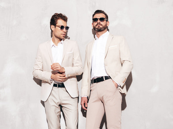Portrait of two handsome confident stylish hipster lambersexual models. Sexy modern men dressed in white elegant suit. Fashion male posing in studio near grey wall in sunglasses